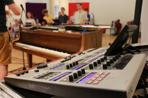 Zu sehen ist ein Mischpult, im Hintergrund erkannt man Mitglieder des Chores